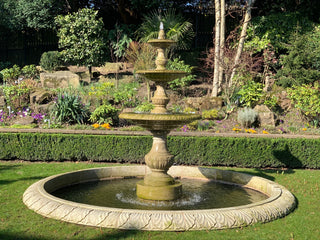 triple tier stone fountain in a garden with assorted plants in the background