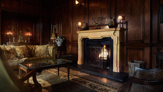 Hand carved stone fireplace with a black marble hearth in a cozy, wood-panelled living room